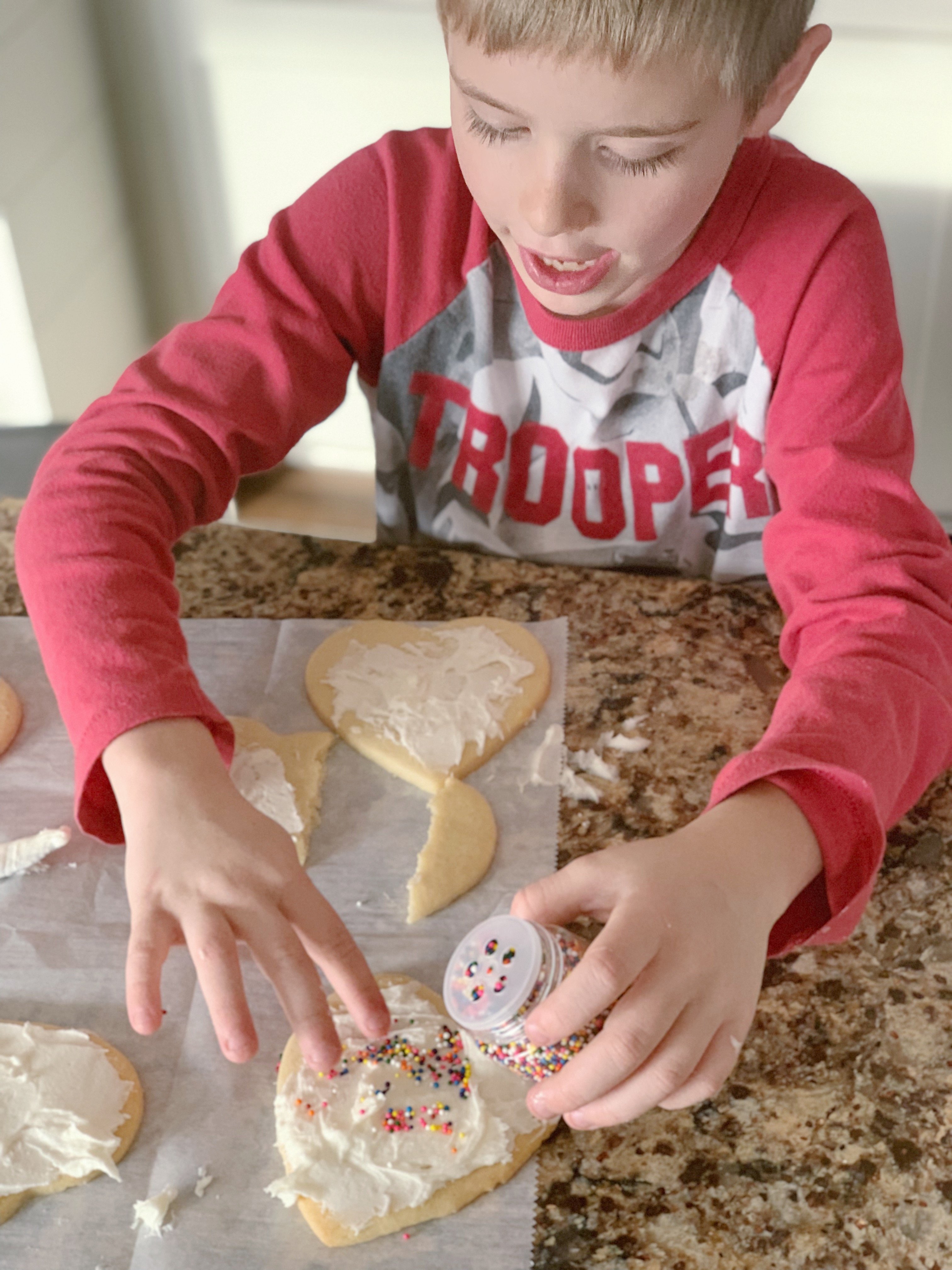 Blonde boy with red and grey shirt decorating sugar cookies.