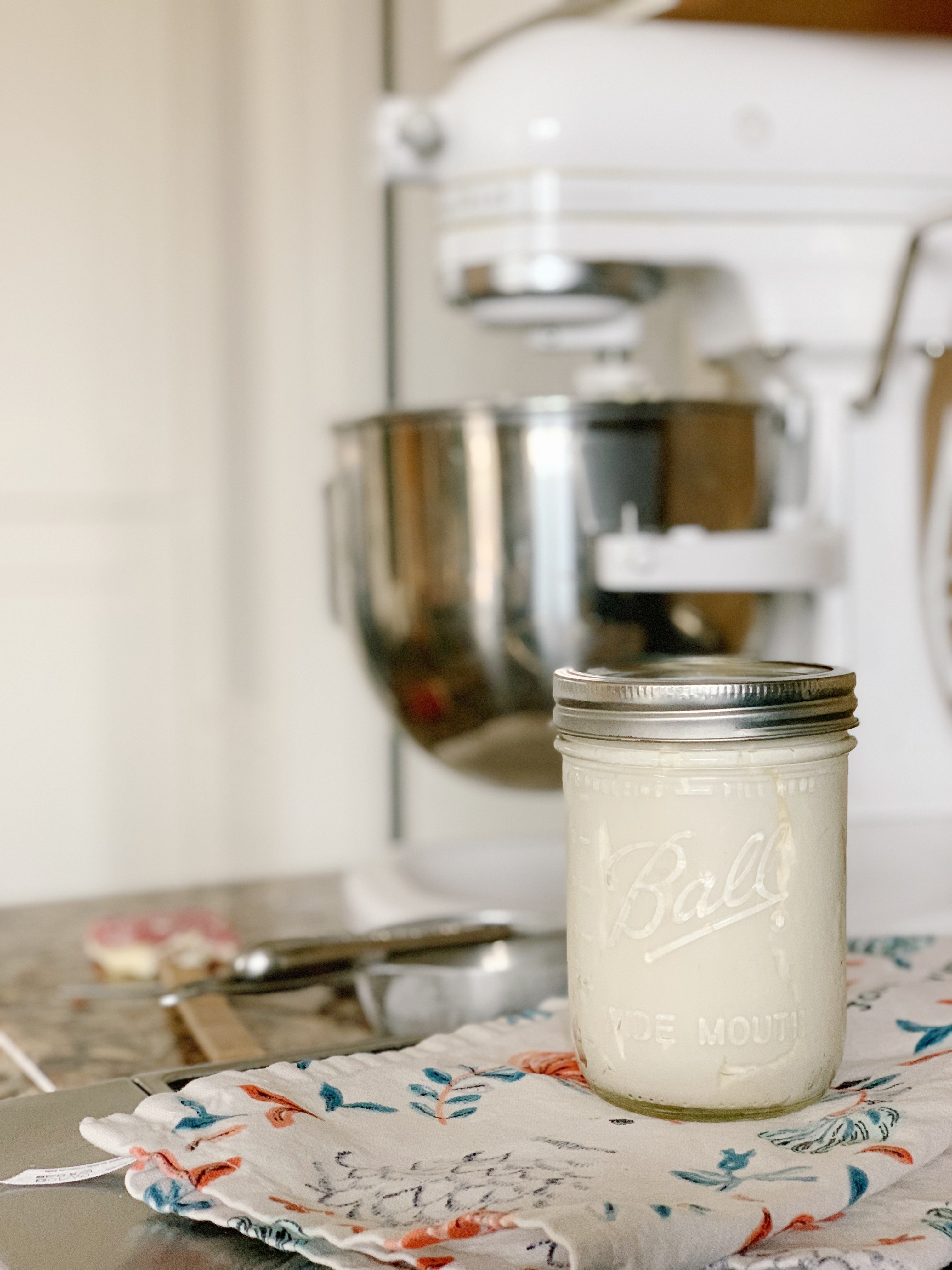 A Ball mason jar full of extra frosting with a blurred mixer in the background. 
