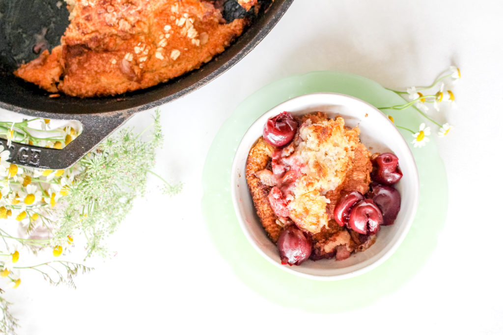 Cobbler served in a jadeite bowl with a cast iron skillet in the background.