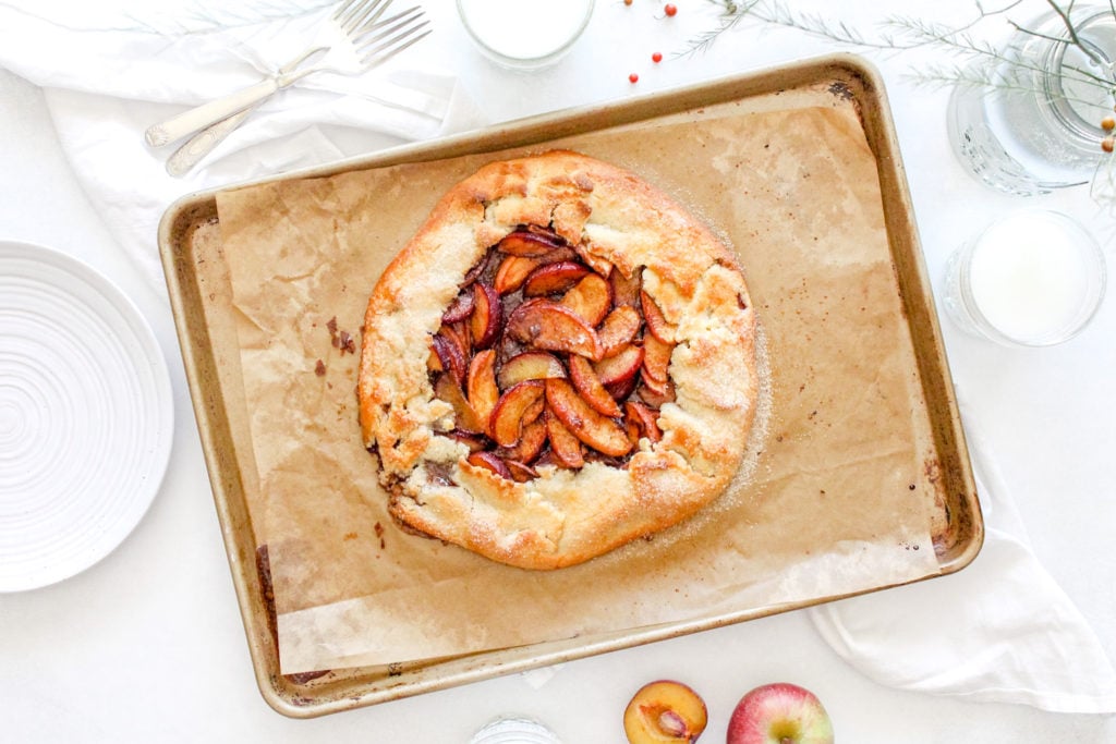 Freshly baked apple and plum gluten free galette on a baking sheet with parchment paper.