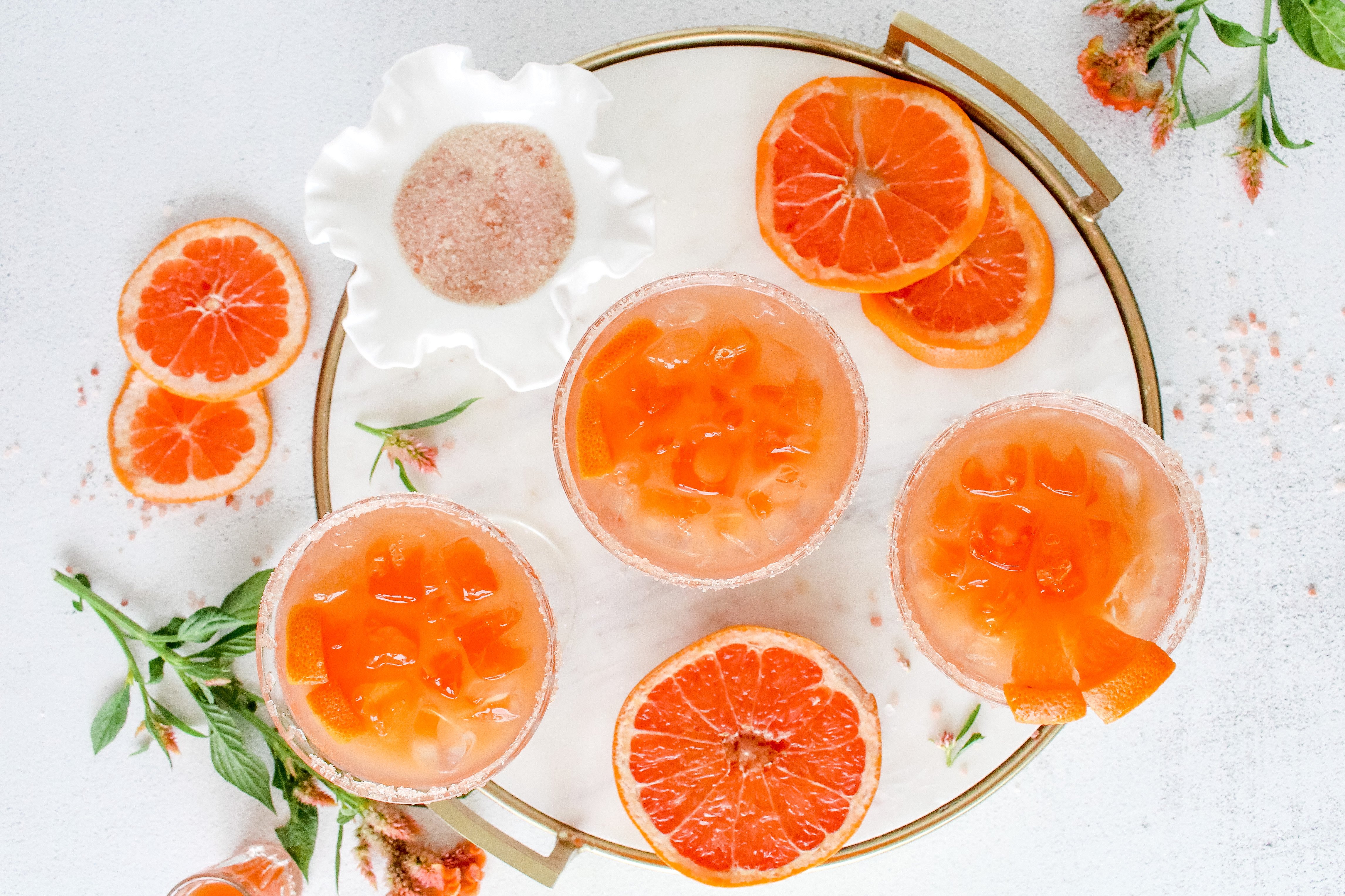 Salty dog cocktails on a marble and brass tray with garnishes and celosia flowers.