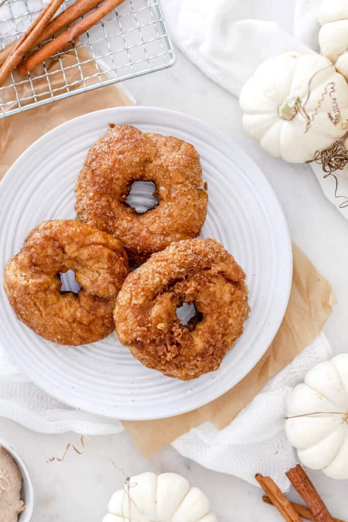 Copycat panera cinnamon crunch bagel, top view, three on a plate with cinnamon sticks and pumpkins.