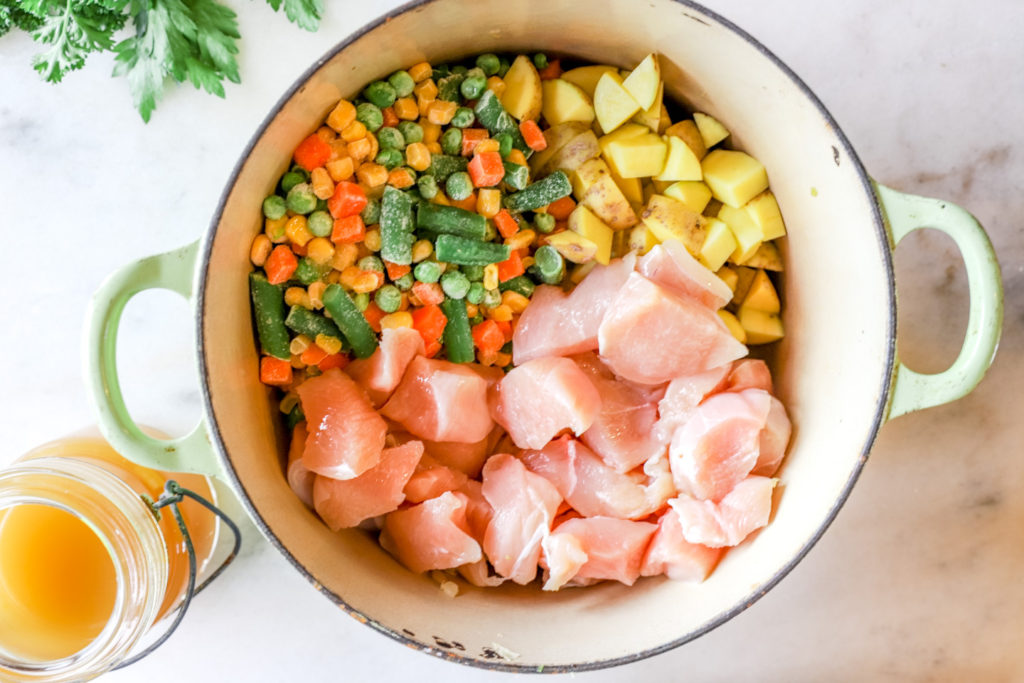 A bright blue dutch oven filled with diced chicken and vegetables to show the process of making a pot pie.