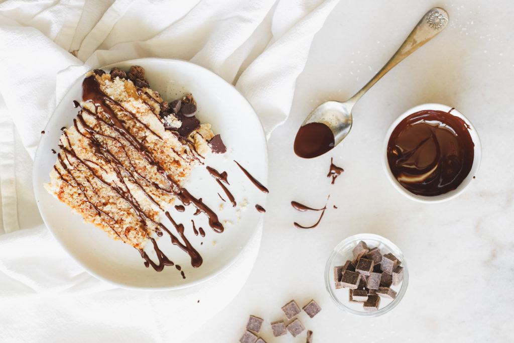 A generous slice of peanut butter cake drizzled with melted fudge and chocolate chunks.