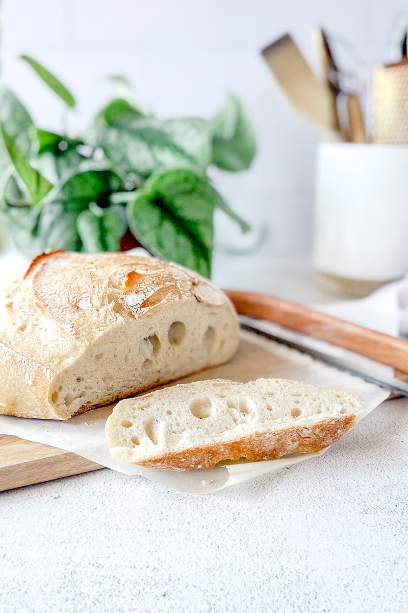 A baked loaf of sourdough that has been freshly sliced on a wood cutting board.