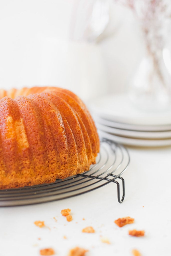 Profile of a buttermilk bundt cake on a cooling rack with plates in the background.