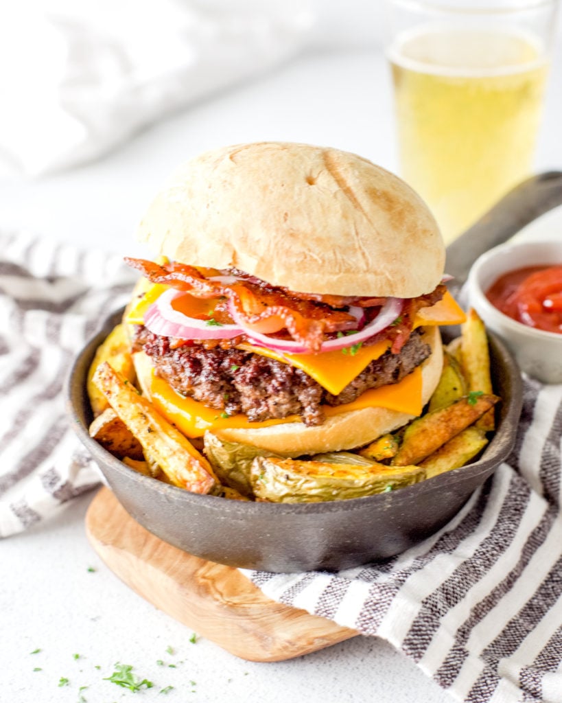 A juicy venison burger layered with crispy bacon and cheddar cheese. It's served in a mini cast iron skillet over a bed of oven fries.