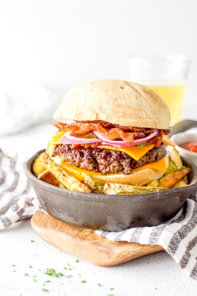 Venison cheddar bacon burger on a sourdough bun served in a mini cast iron skillet over a bed of freshly baked oven fries.