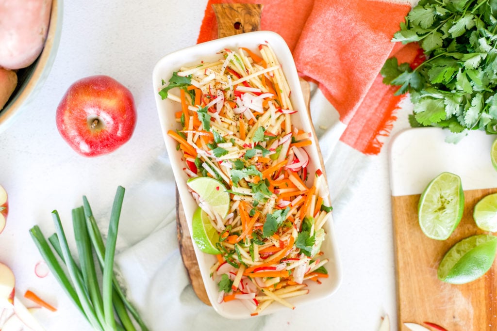 A platter of apple slaw on a brightly colored napkin with apple and scallion garnishes.