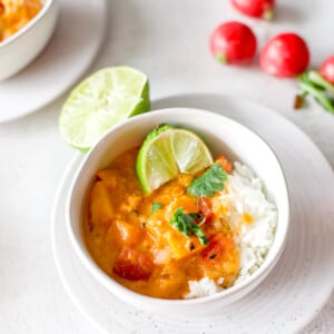 A bowl of fresh butternut curry with lime wedges and cilantro garnishes.