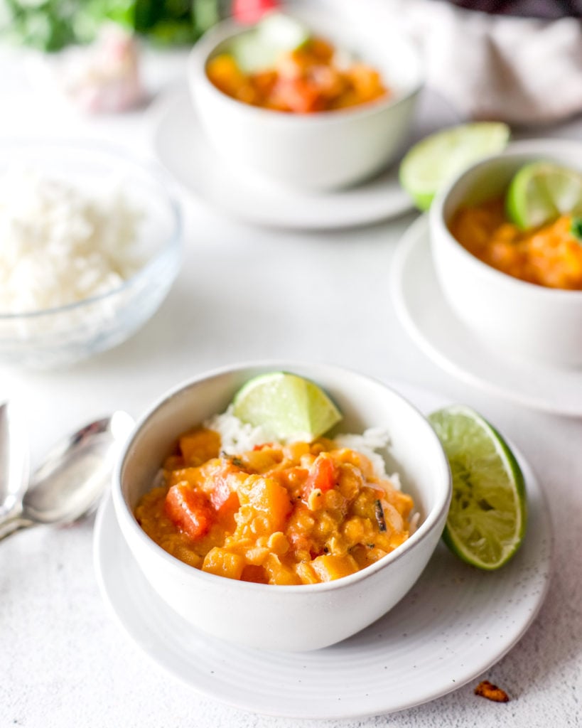 A bowl of hot red butternut squash curry with lime wedge garnishes.