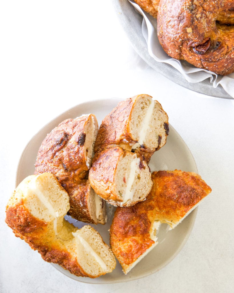 Sourdough bagels sliced and filled with cream cheese on a white plate.