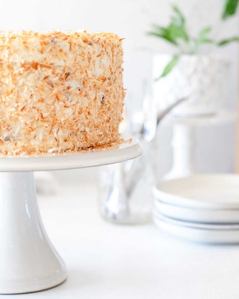 Profile of a coconut crusted Old Fashioned Italian cream cake on a white serving stand.