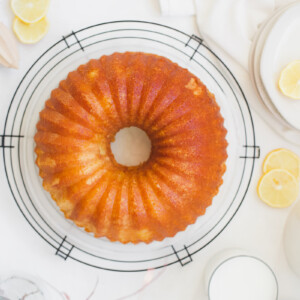 lemon buttermilk bundt cake on a cooling rack garnished with lemons and fresh pink flowers