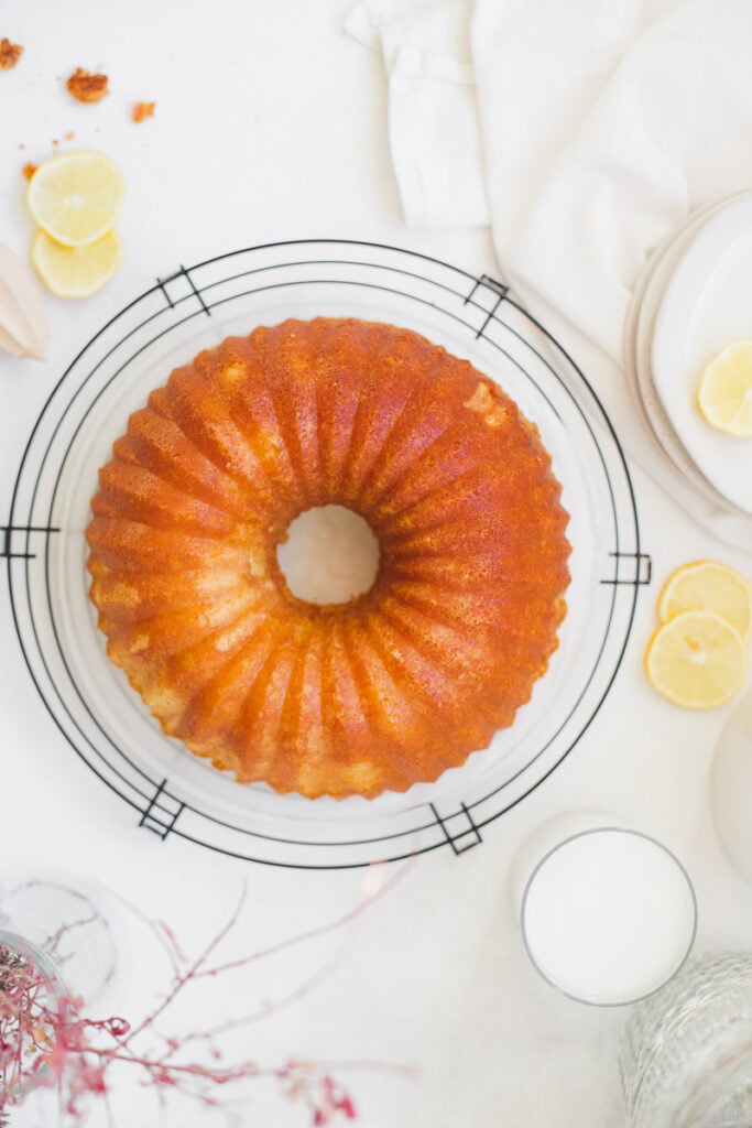 lemon buttermilk bundt cake on a cooling rack garnished with lemons and fresh pink flowers