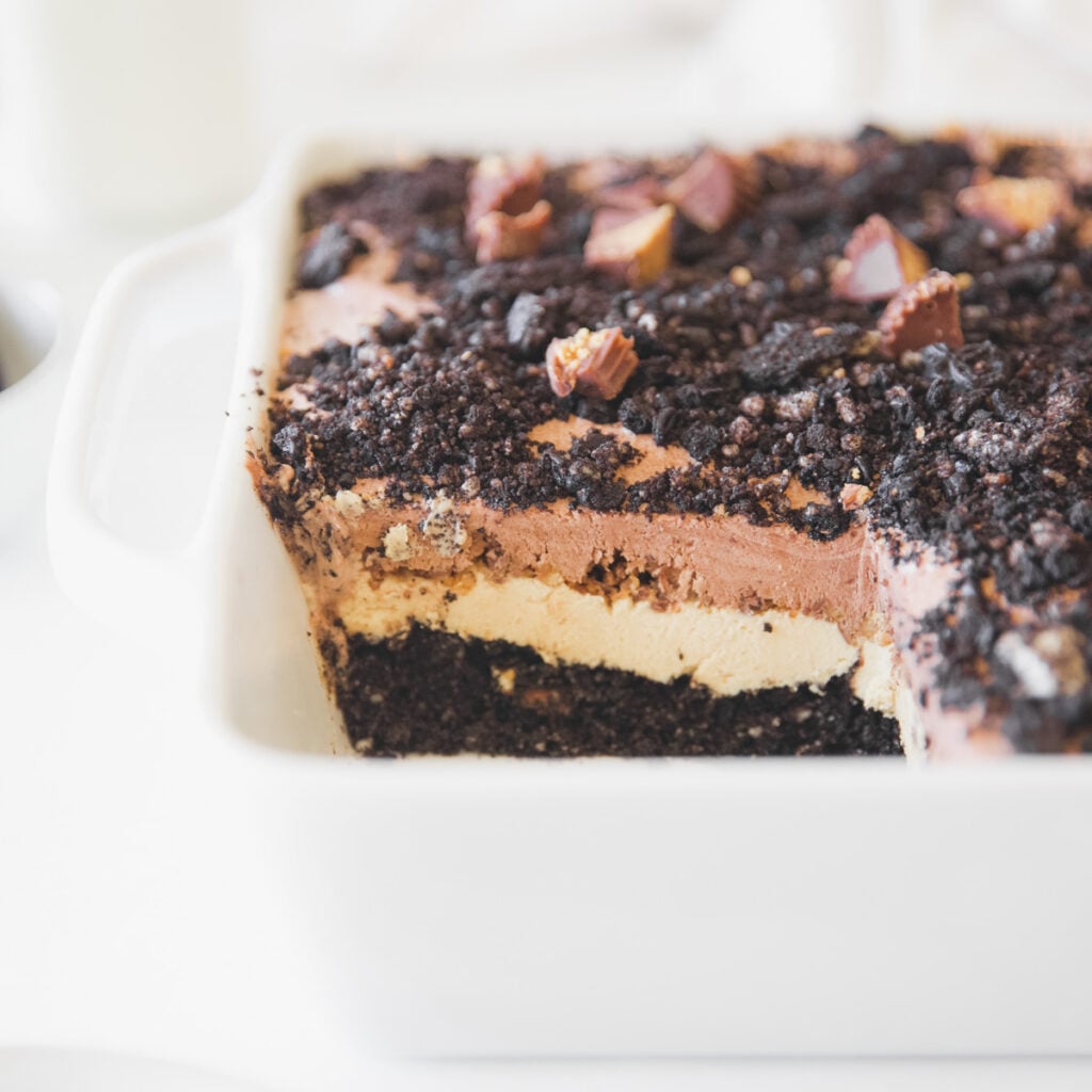 An oreo icebox cake that has had a corner piece removed and the inner layers of peanut butter and chocolate pudding are exposed.