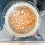 The simmering mixture of honey and water on a stovetop.