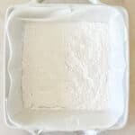 A line baking dish with parchment and powdered sugar ready for marshmallow filling.