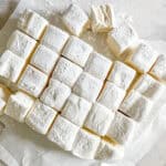 A parchment paper with squares of homemade marshmallows without corn syrup dusted in powdered sugar.