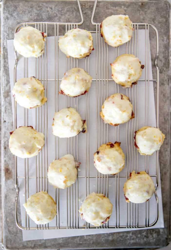 A wire cooling rack with freshly iced cranberry orange cookies evenly spaced over parchment paper.