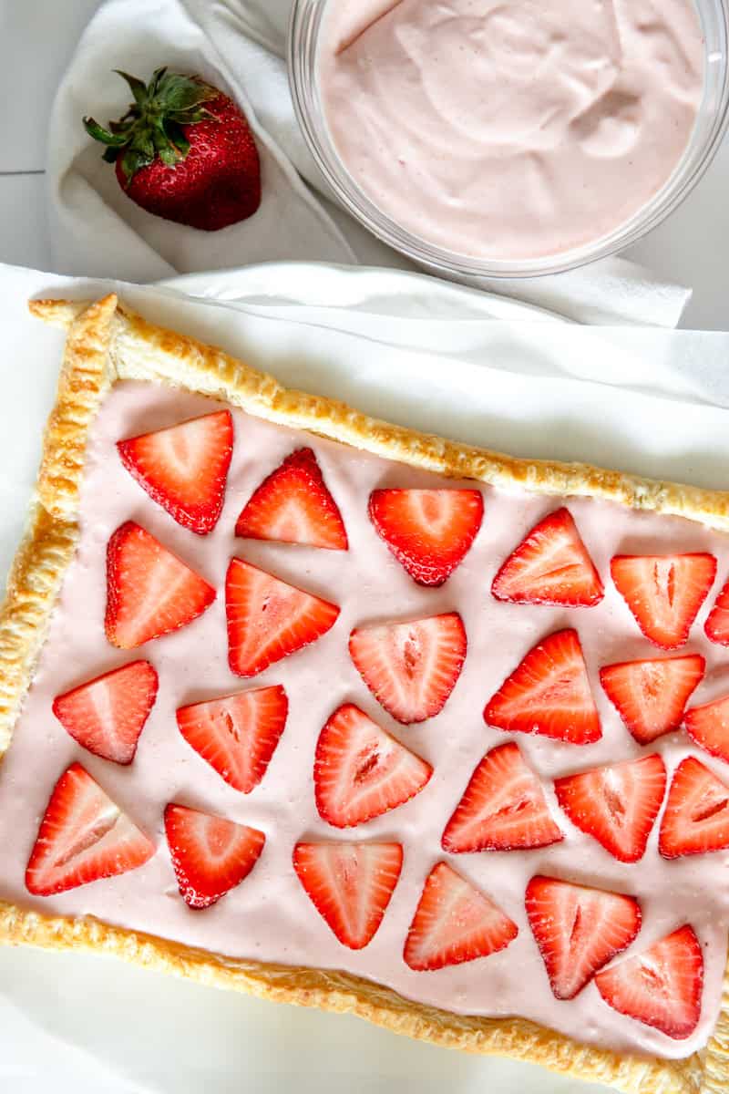 A strawberry cheesecake tart with sliced fresh strawberries and pink cheesecake filling on a white platter.