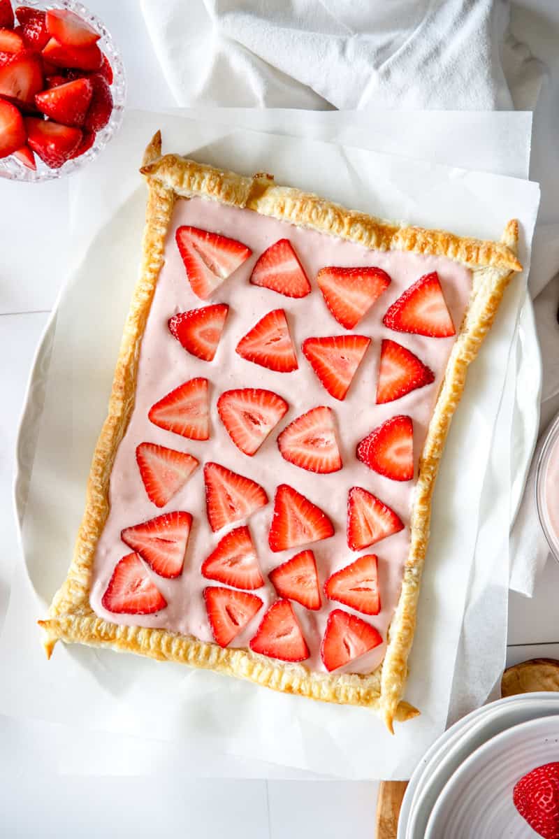 A strawberry cheesecake tart on a white platter with white linens showing thinly sliced strawberries.