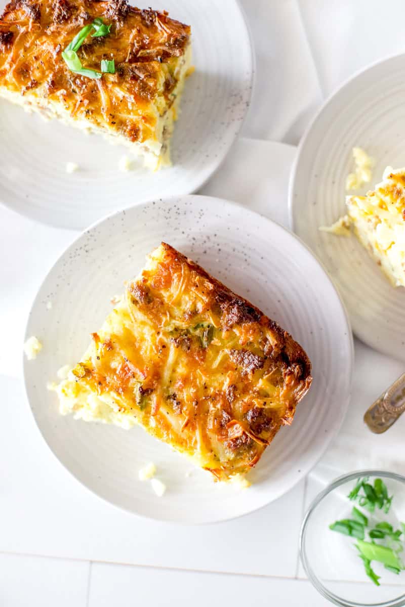 A Birdseye view of breakfast casserole slices on white plates served garnished with green onions.