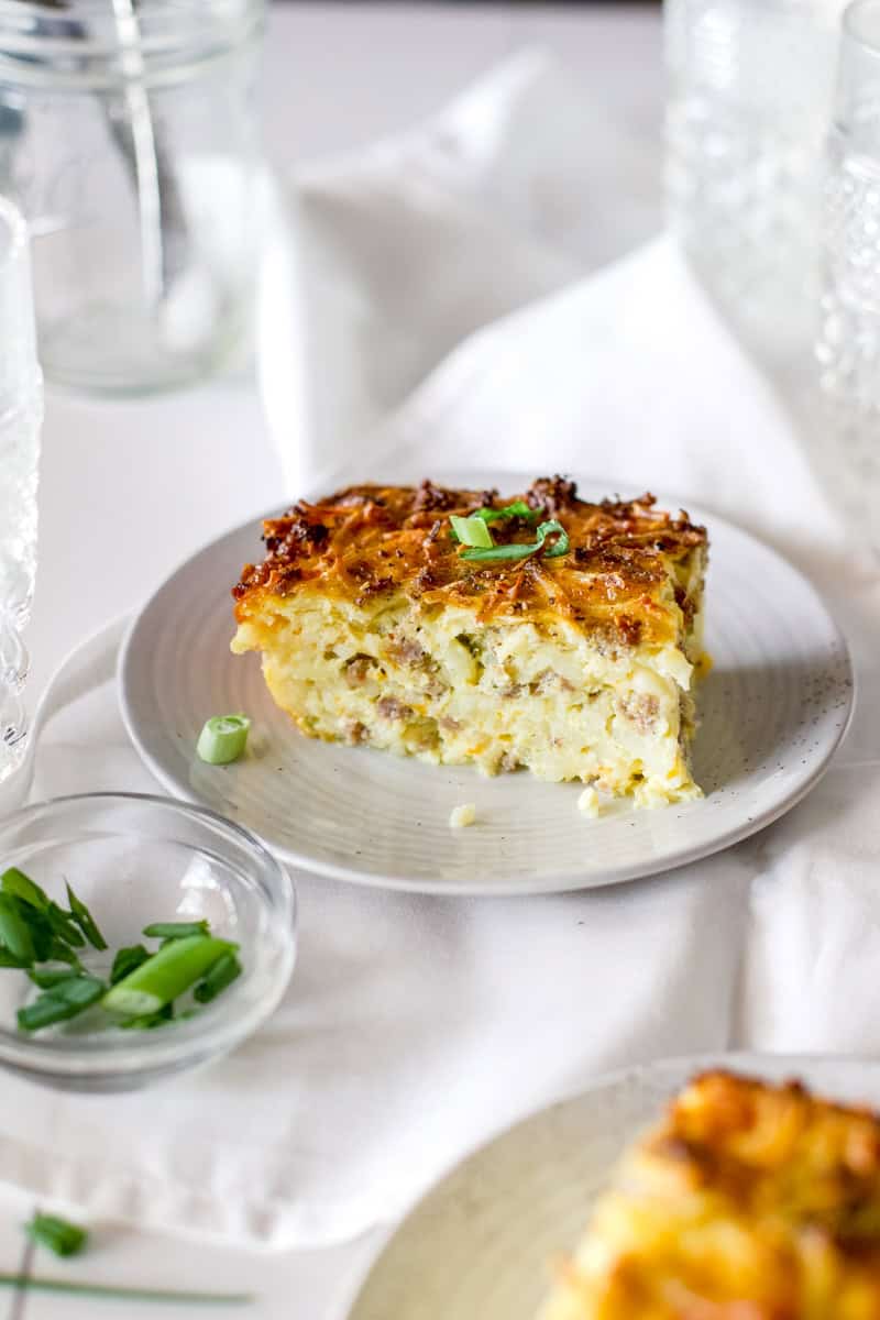 A slice of venison breakfast casserole on a. white dish garnished with green onions and white linens.