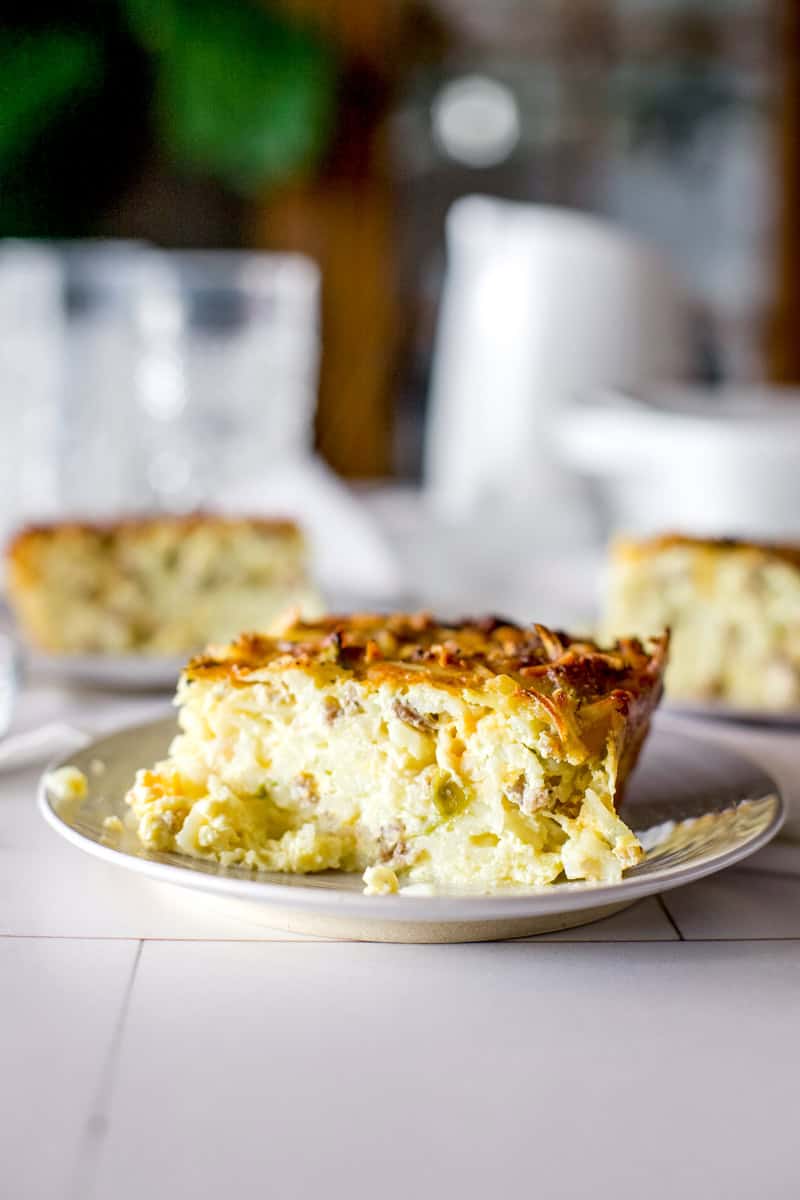 A slice of venison breakfast casserole on a white plate with milk and glasses in the background.