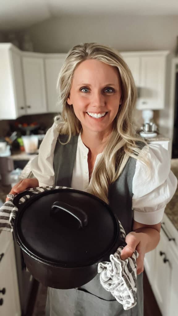 A smiling chef holding a dutch oven of chicken broth.