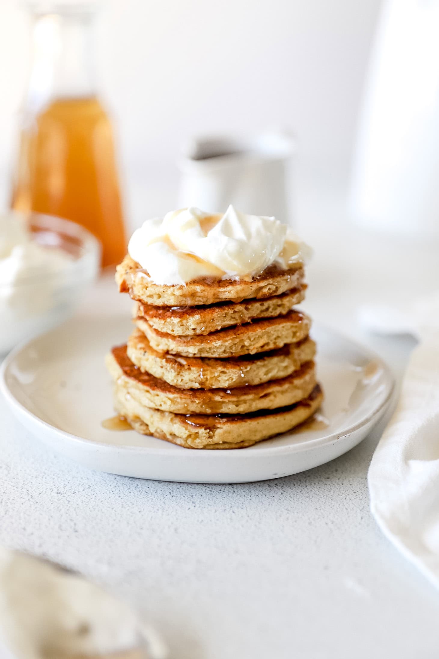 A stack of sourdough pancakes on a white plate piled high with whipped cream.