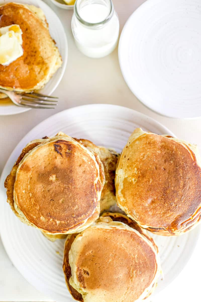 A plate filled with stacks of pancakes on a white backdrop with milk glasses.