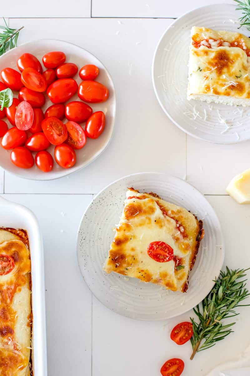 A flat lay of sourdough pizza bread sliced into squares and served on white plates.