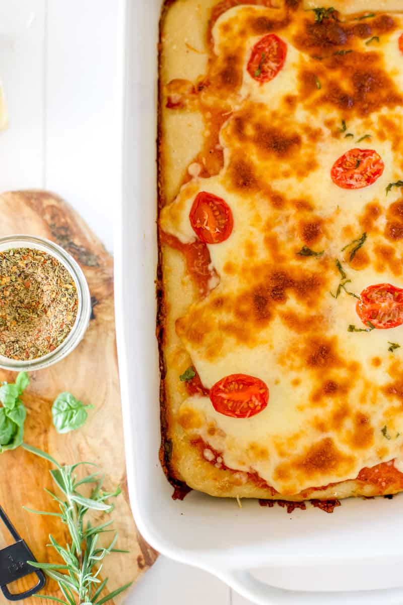 Sourdough Pizza bread with tomatoes and mozzarella in a white ceramic baking dish garnished with basil.