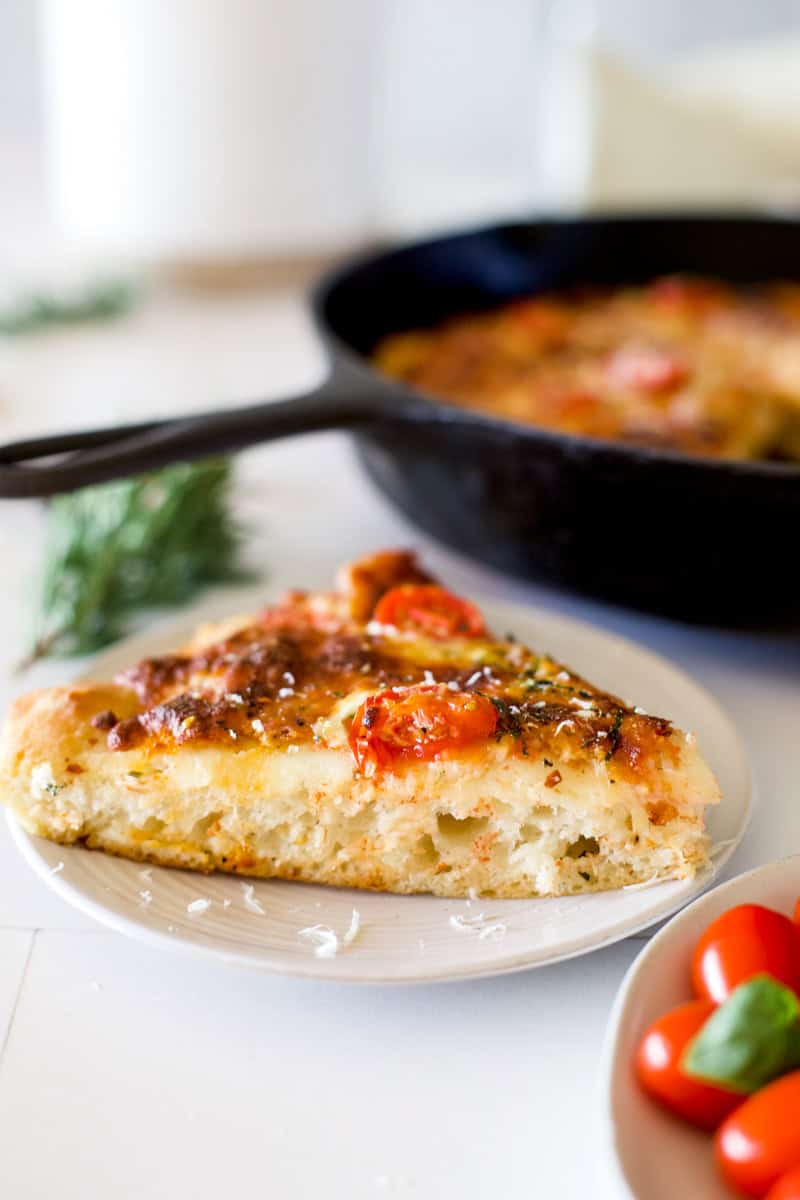 A slice of sourdough pizza, deep dish style with cheese and garden fresh tomatoes.