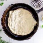 A cast iron skillet with sourdough pizza crust dough resting before baking.