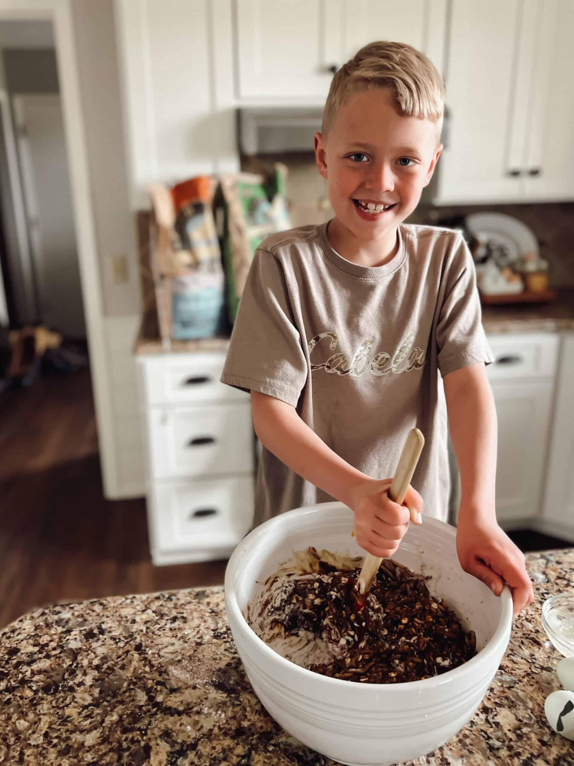 A boy smiling as he mixes a bowl filled with mealworms, molasses, chicken feed and whole grains to make a flock block for his pet chickens.