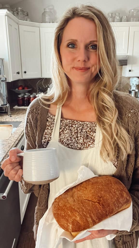 Meg holding fresh bread and coffee wearing an apron.