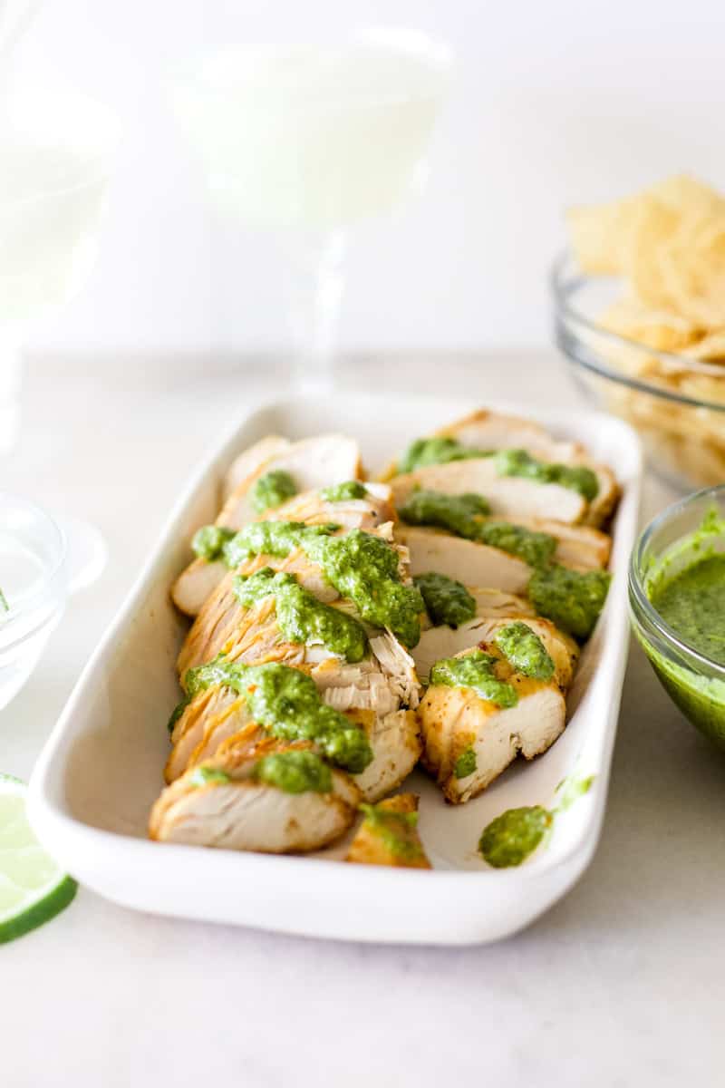 An air fried chicken breast on a white platter that has been thinly sliced and topped with chimichurri sauce.