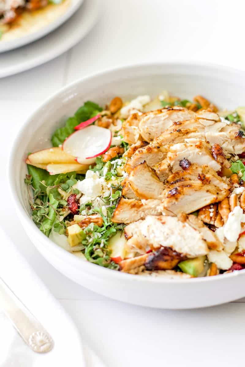 A large salad in a white bowl topped with air fryer chicken breasts sliced thinly.