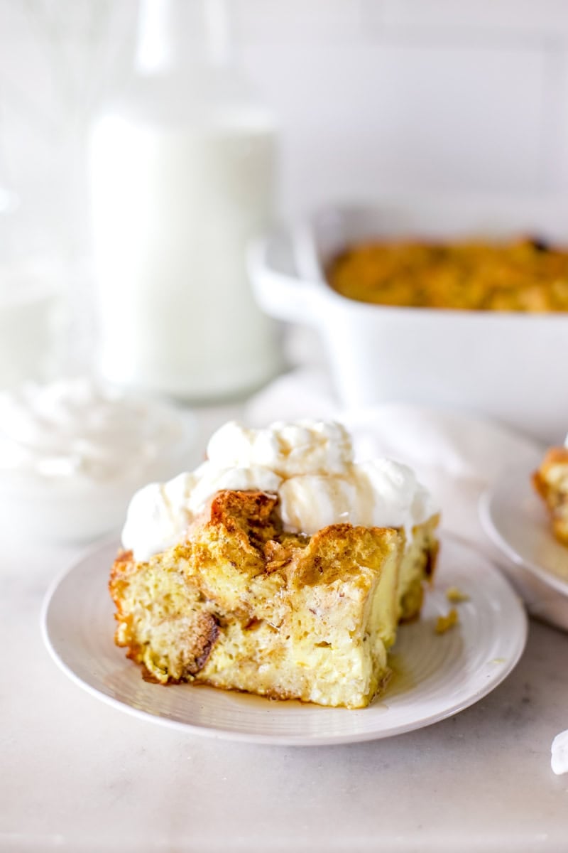 A styled image of a slice of bread pudding drizzled with caramel sauce and a dollop of whipped cream on top.