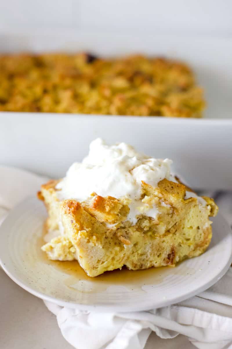 An up-close picture of a slice of sourdough bread pudding with whipped topping on a white plate.