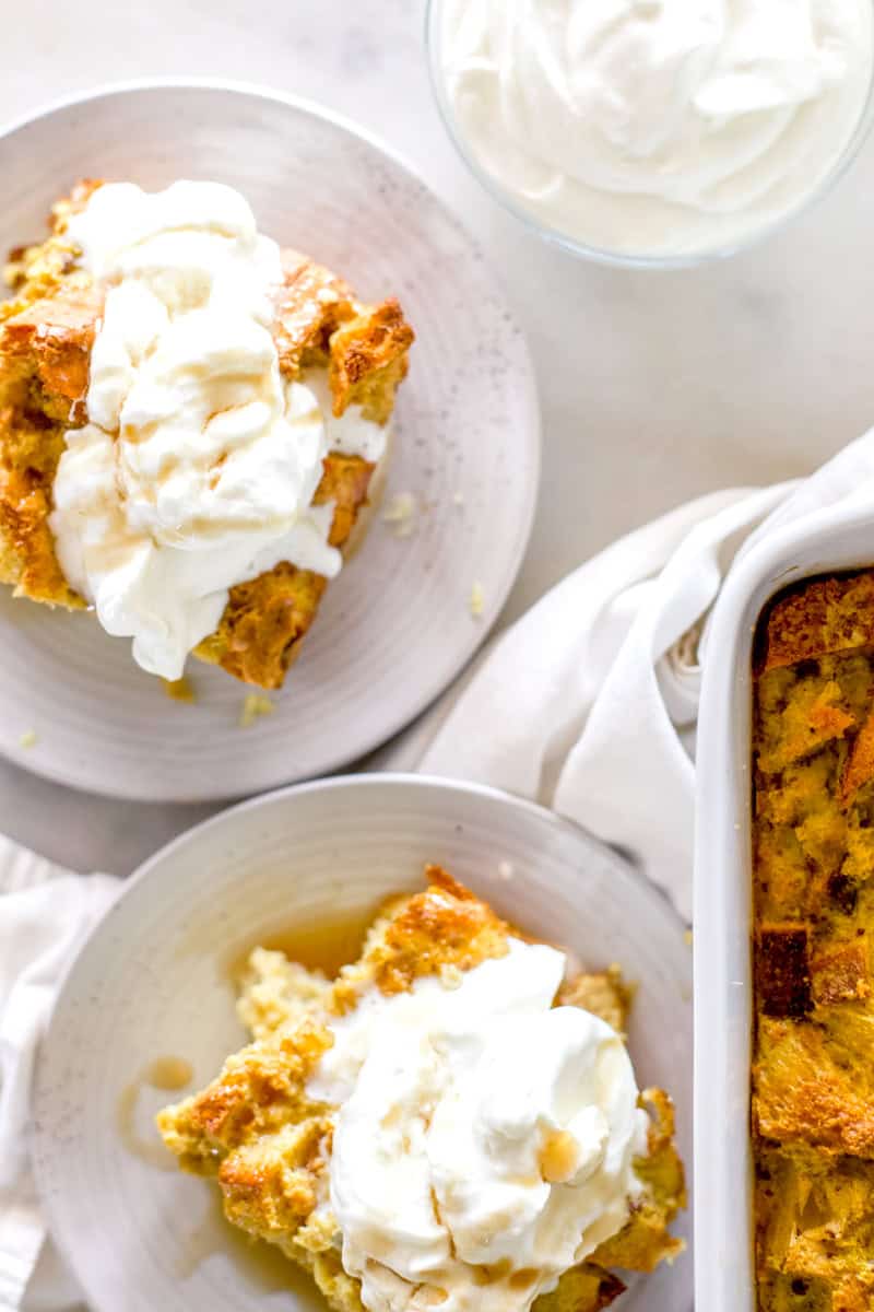 A top view of two servings of sourdough bread pudding piled high with dollops of whipped cream and drizzled with caramel sauce.