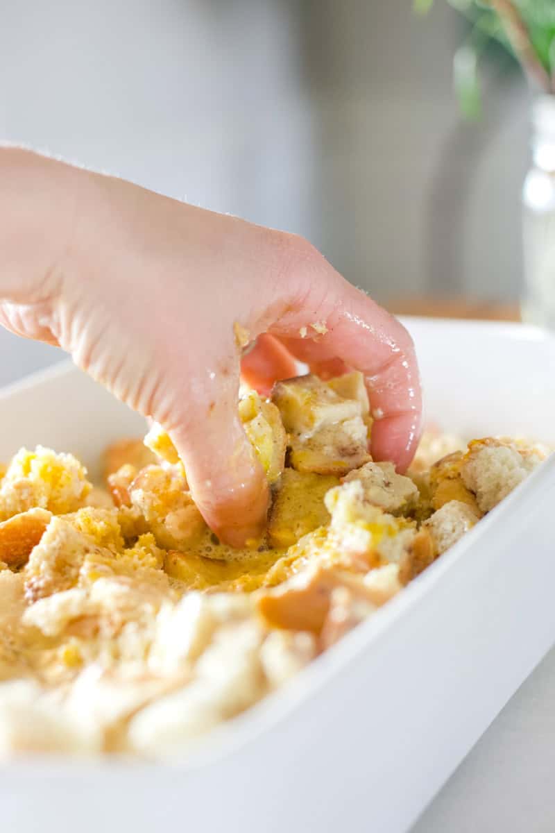 Step four of making sourdough bread pudding: Use your clean hands to squish the egg mixture and the bread pieces together. Pat it down into an even layer.