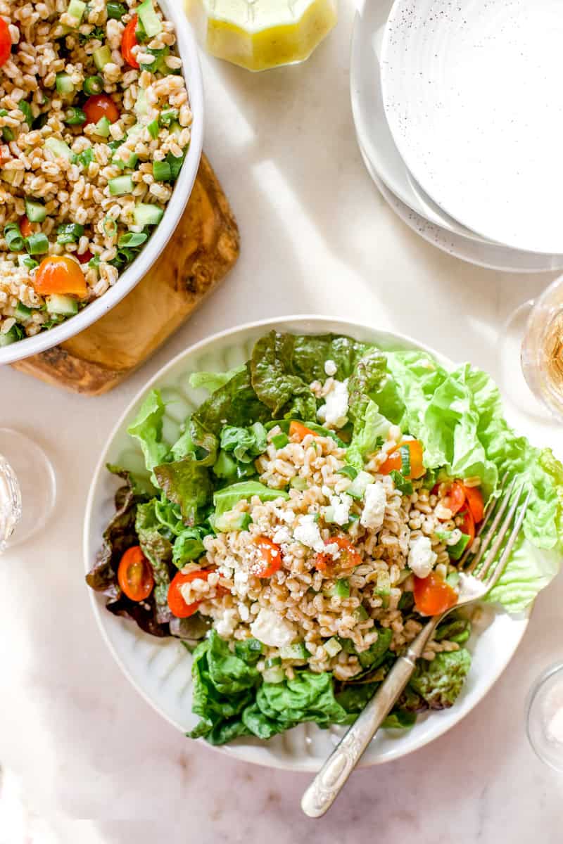 A salad topped with farro and finely chopped cucumbers, parsley, cherry tomatoes, and served with tabbouleh.