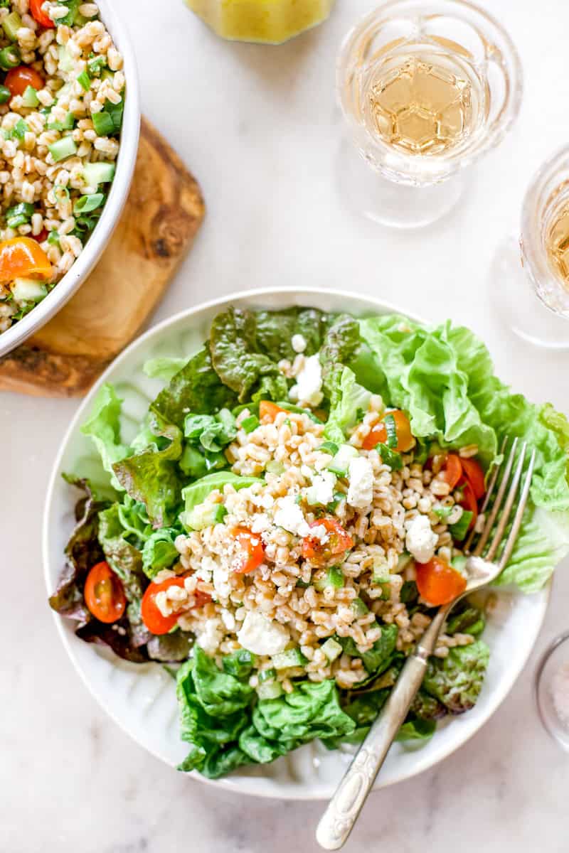 A large plate filled with colorful leaf lettuce and topped with feta, cucumber, lemon, farro and lemon cucumber salad.