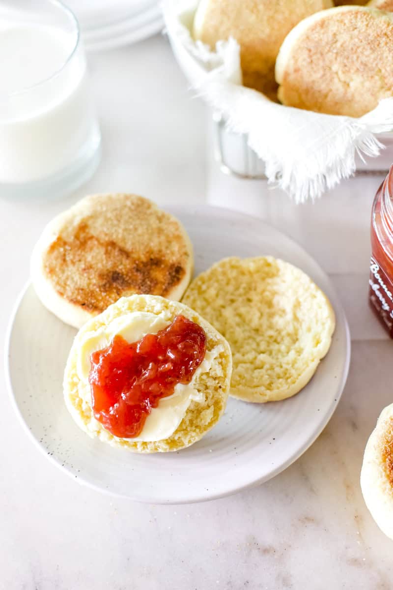 A cooked sourdough English muffin with jelly and butter on a white plate.