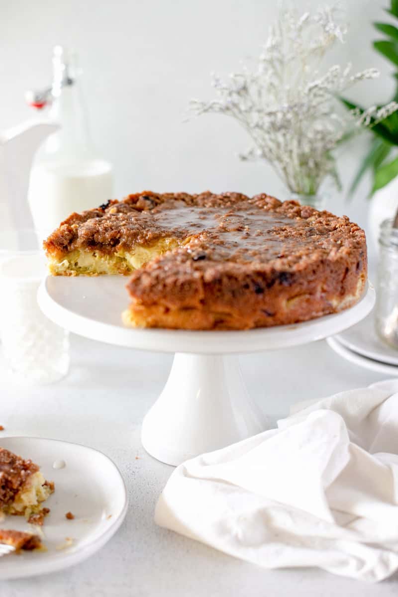 Rhubarb sour cream coffee cake on a white cake stand with a piece served on a white plate.