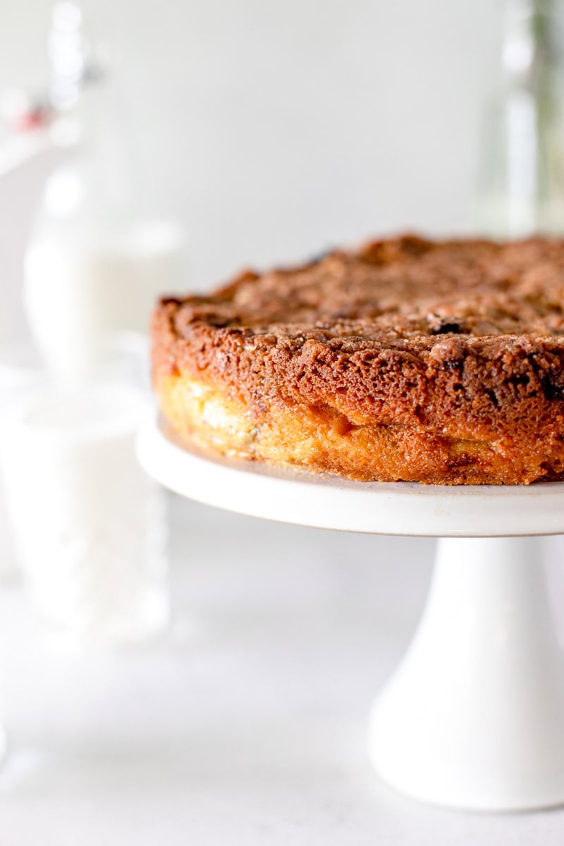 A side view of a rhubarb sour cream cake on a white pedestal, showing the detail of the crust and crumble topping.