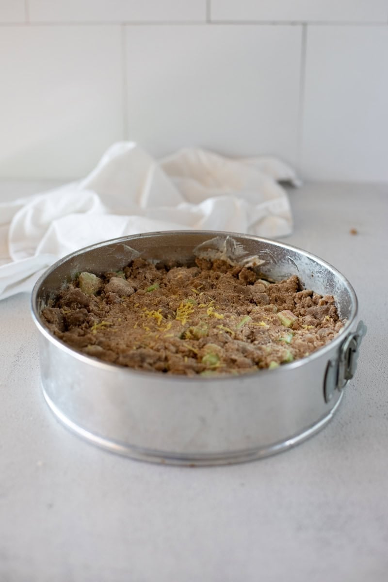 Step 5 of making a rhubarb sour cream cake is layering the cake batter and crumble topping into a prepared springform pan.